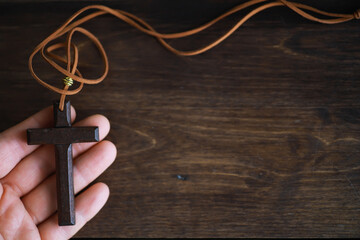 Hand Holding Wooden Cross Necklace Against Dark Wooden Background