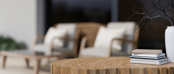 A close-up of a wooden table featuring books and a minimal ceramic vase