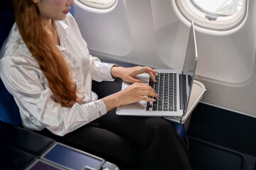 A close-up of a businesswoman typing on the laptop keyboard, working during the flight.
