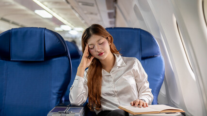 A tired Asian businesswoman feels dizzy from reading during the long flight, traveling abroad.