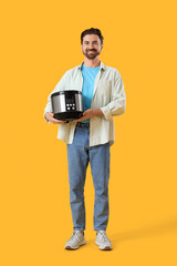 Young man with multi cooker on yellow background
