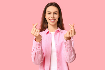 Beautiful young woman making heart gesture on pink background