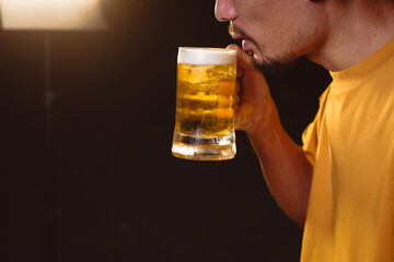A man's hand lifts a beer glass in the quiet aftermath of a night party, capturing a solitary moment of reflection under dim lights and the lingering echo of celebration.