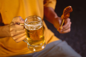 A man's hand lifts a beer glass in the quiet aftermath of a night party, capturing a solitary moment of reflection under dim lights and the lingering echo of celebration.
