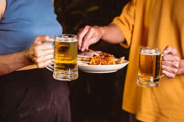 A man's and woman's hands raise beer glasses group in a lively night party, surrounded by family and friends. The evening is filled with warmth, laughter, and joyful celebration.