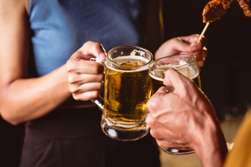 A man's and woman's hands raise beer glasses group in a lively night party, surrounded by family and friends. The evening is filled with warmth, laughter, and joyful celebration.
