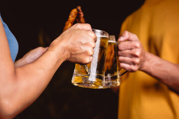 A man's and woman's hands raise beer glasses group in a lively night party, surrounded by family and friends. The evening is filled with warmth, laughter, and joyful celebration.