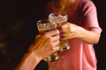 A man's and woman's hands raise beer glasses group in a lively night party, surrounded by family and friends. The evening is filled with warmth, laughter, and joyful celebration.