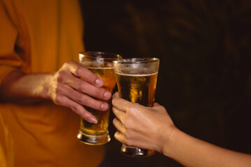 A man's and woman's hands raise beer glasses group in a lively night party, surrounded by family and friends. The evening is filled with warmth, laughter, and joyful celebration.