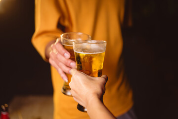 A man's and woman's hands raise beer glasses group in a lively night party, surrounded by family and friends. The evening is filled with warmth, laughter, and joyful celebration.