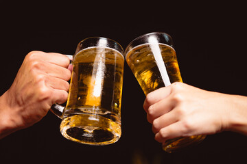 A man's and woman's hands raise beer glasses group in a lively night party, surrounded by family and friends. The evening is filled with warmth, laughter, and joyful celebration.
