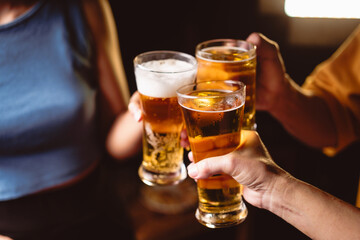 A man's and woman's hands raise beer glasses group in a lively night party, surrounded by family and friends. The evening is filled with warmth, laughter, and joyful celebration.