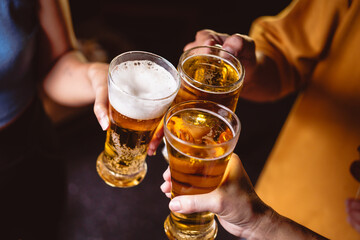 A man's and woman's hands raise beer glasses group in a lively night party, surrounded by family and friends. The evening is filled with warmth, laughter, and joyful celebration.