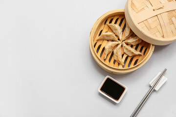 Bamboo steamer with tasty Japanese gyoza and bowl of soy sauce on grey background