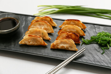 Black board of fried Japanese gyoza with seaweed salad and and bowl of soy sauce on grey background