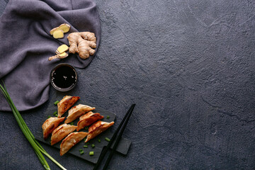 Black board with fried Japanese gyoza and bowl of soy sauce on dark background