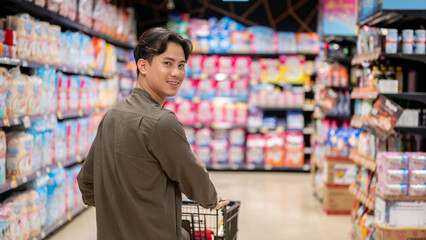 A smiling Asian man shopping at a supermarket, walking through an aisle, and smiling at the camera.