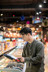 A man selecting frozen items from a freezer while shopping at a supermarket, buying his groceries.