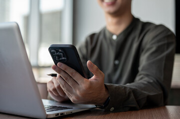 A close-up of a smiling Asian businessman using his smartphone while working in a modern office.