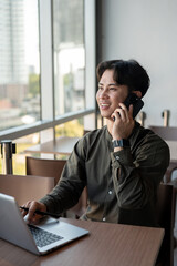 Obraz premium A positive Asian businessman talking on the phone while working remotely from a coffee shop.