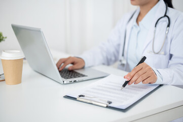 A close-up of a doctor working at her desk, typing on the laptop keyboard, reading medical paper.