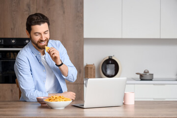 Man with laptop eating tasty nachos in kitchen