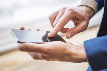 Man engaged with his modern smartphone out of focus nearby against the blurred office hustle and...