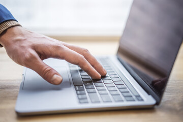 Set against a blurred office scene, the image reveals a close-up of a man's hands typing on a modern laptop keyboard