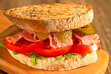 View Close-up of Delicious Sandwich with Ham Salami, Pickled Cucumbers, Fresh Vegetables on Rustic Wooden Cutting Board At Wooden Table, Selective Focus.