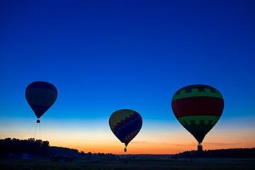 Obraz premium Three Mesmerizing Colorful Air Balloons Levitating Over the Ground Outdoors Against Clear Blue Skies At Twilight.