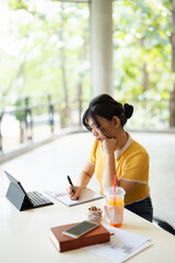 Stressed girl making notes in exercise book sitting at cafeteria table, Concentrated student...