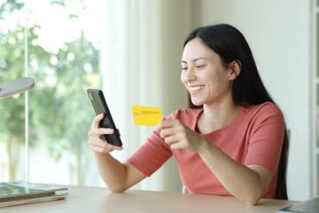 Happy asian woman buying online in a room