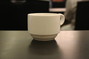 Plain white ceramic cup with handle, dark table, soft light indoor, blurred background.