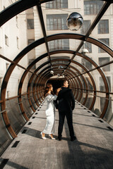 couple standing in a glass corridor with arched metal structures.