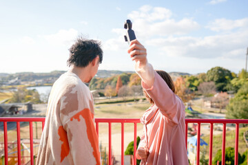 At a large park in Handa City, Aichi Prefecture, a couple in their 20s are having fun playing on the playground equipment and taking selfies with a small camera.