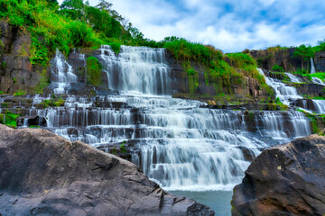 Fototapeta premium Mystical waterfall with foreground is autumn leaves in the Da Lat plateau, Vietnam. This is known as the first Southeast Asian waterfall in the wild attracted many tourists to visit