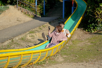 In a large park in Handa City, Aichi Prefecture, a couple in their 20s are having fun on the slide while taking selfies with a small camera.