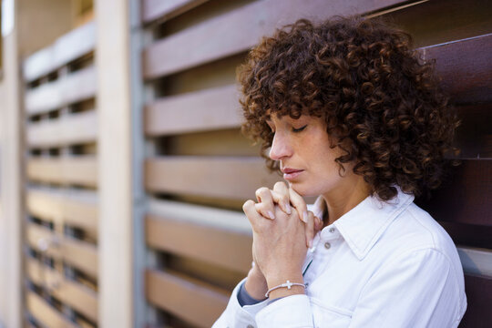Woman with curly hair praying near wooden wall