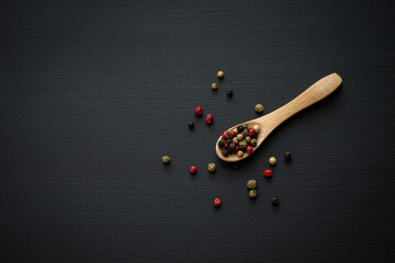colorful peppercorns lie on a wooden spoon on a black background