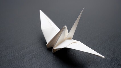 Delicate white origami crane positioned on dark surface, symbolizing peace and hope with intricate folds and sharp angles.