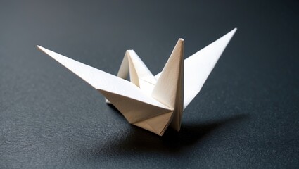 Origami crane crafted from white paper, showcasing intricate folds and sharp angles, set against a dark background.