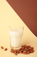 Fresh almond milk in glass and almonds on beige background. Healthy vegan plant based alternative milk replacer. Vertical photo