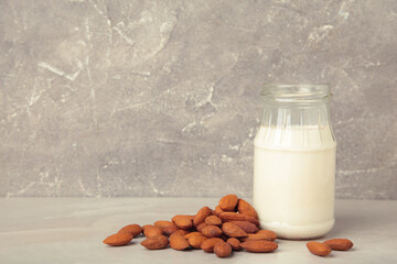 Fresh almond milk in glass bottle and almonds on grey background. Healthy vegan plant based alternative milk replacer. Vertical photo