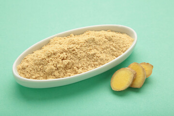 Ginger powder on white plate with fresh ginger root on mint background. Top view
