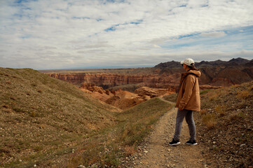female tourist on the trail looking at the beautiful orange canyon mountains and cloudy sky