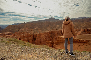 female tourist on the trail looking at the beautiful orange canyon mountains and cloudy sky
