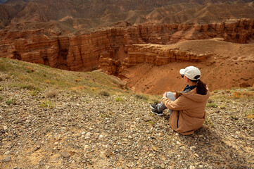 female tourist sits on a hill and looks at the beautiful orange canyon mountains and cloudy sky