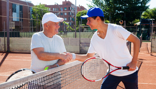 Mature senior and young man shake hands before tennis match