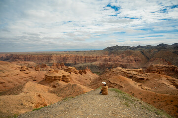 female tourist sits on a hill and looks at the beautiful orange mountains canyons, rear view