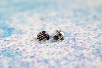 Silver handmade earrings with gemstones in shell and starfish shapes on sparkly background.